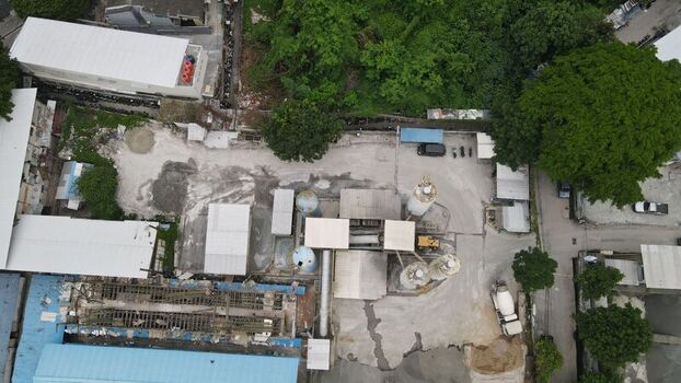 Aerial view of a concrete batching plant with industrial silos a mixer truck and storage areas surrounded by trees and buildings in Kecamatan Menteng Daerah Khusus Ibukota Indonesia. Aerial view of a concrete batching plant with industrial silos a mixer truck and storage areas surrounded by trees and buildings in Kecamatan Menteng Daerah Khusus Ibukota Indonesia.