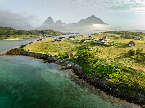 Aerial view of the lush green landscape of Lofoten in summer featuring scattered traditional houses rocky coastlines and clear turquoise waters in Lofoten Norway.