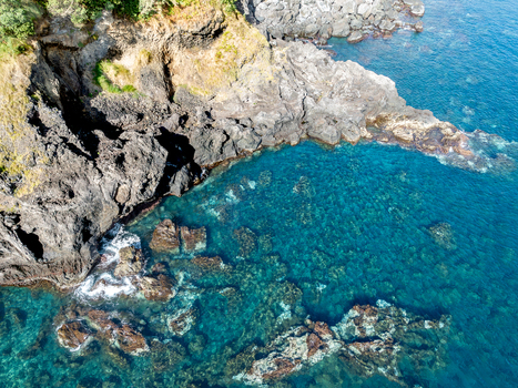 Aerial view of the rugged volcanic coastline with crystal clear turquoise water and dark rock formations Ribeira Grande Azores Portugal.