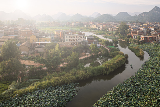 Aerial view of Puzhehei Scenic Spot with a winding river lotus fields and village architecture set against karst mountains in Wenshan Zhuang and Miao Autonomous Prefecture China.