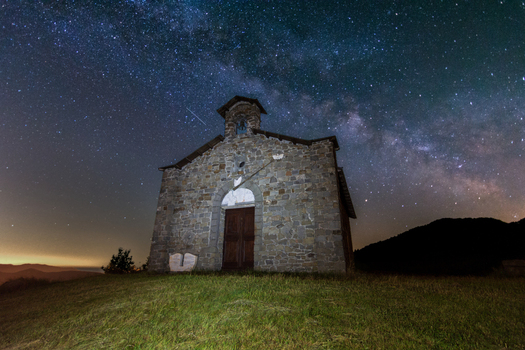View of the small stone chapel at Passo di Cirone under a vibrant Milky Way and starry night sky on a grassy hilltop in Pontremoli Toscana Italy. View of the small stone chapel at Passo di Cirone under a vibrant Milky Way and starry night sky on a grassy hilltop in Pontremoli Toscana Italy.