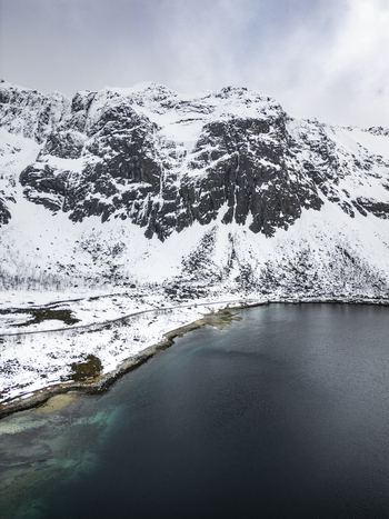 Aerial view of Grotfjord with snow covered mountains and dark blue water under a cloudy sky in Tromvik Troms Norway. Aerial view of Grotfjord with snow covered mountains and dark blue water under a cloudy sky in Tromvik Troms Norway.