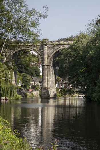 View of the historic Knaresborough Viaduct spanning the River Nidd surrounded by lush green trees and reflecting in the calm water in Knaresborough England United Kingdom.