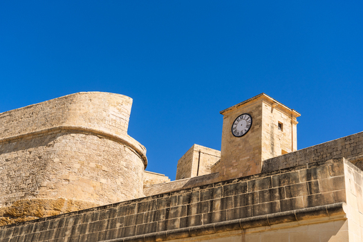 View of historic limestone fortifications and a clock tower under a clear blue sky in Zebbug Gozo Region Malta. View of historic limestone fortifications and a clock tower under a clear blue sky in Zebbug Gozo Region Malta.