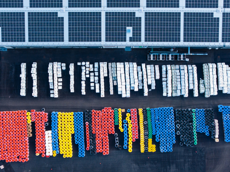 Aerial view of a manufacturing facility yard featuring rows of colorful plastic pipe coils and palletized goods stored next to a building with solar panels in Jelgava Latvia. Aerial view of a manufacturing facility yard featuring rows of colorful plastic pipe coils and palletized goods stored next to a building with solar panels in Jelgava Latvia.