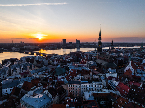 Aerial view of Vecriga the historic old town of Riga featuring the iconic spire of St. Peters Church dense rooftops and the Daugava River under a vibrant sunset sky in Riga Latvia. Aerial view of Vecriga the historic old town of Riga featuring the iconic spire of St. Peters Church dense rooftops and the Daugava River under a vibrant sunset sky in Riga Latvia.