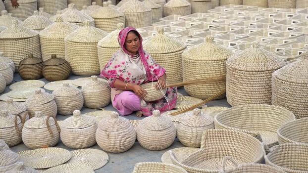 View of a woman weaving traditional baskets in Bangladesh. View of a woman weaving traditional baskets in Bangladesh.
