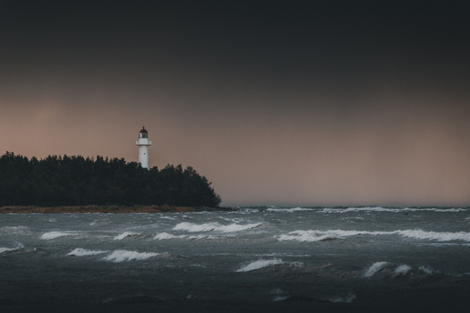 View of Saxby Lighthouse standing on a forested coastline overlooking a stormy sea under a dark moody sky in Saxby Laane maakond Estonia.