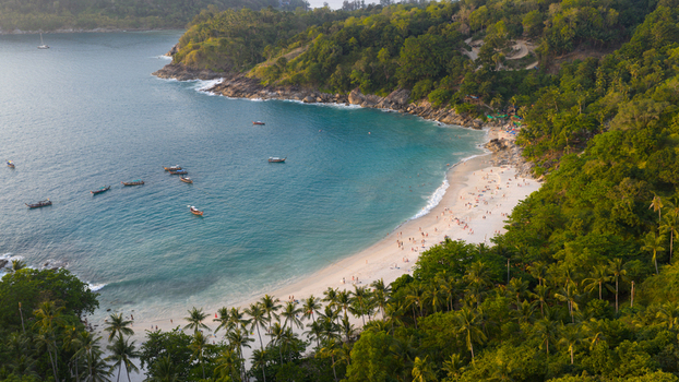Aerial view of Freedom Beach featuring white sand turquoise water longtail boats and lush green jungle in Tambon Patong Chang Wat Phuket Thailand.