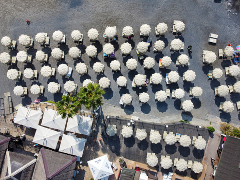 Aerial view of neat rows of white beach umbrellas and sunbeds on a pebble beach with palm trees and a wooden terrace Imperia Liguria Italy. Aerial view of neat rows of white beach umbrellas and sunbeds on a pebble beach with palm trees and a wooden terrace Imperia Liguria Italy.