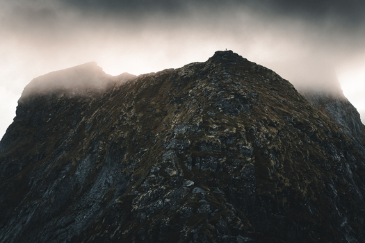 View of the rocky peak of Reinebringen mountain with mossy slopes and dramatic clouds under moody lighting in Moskenes Nordland Norway.
