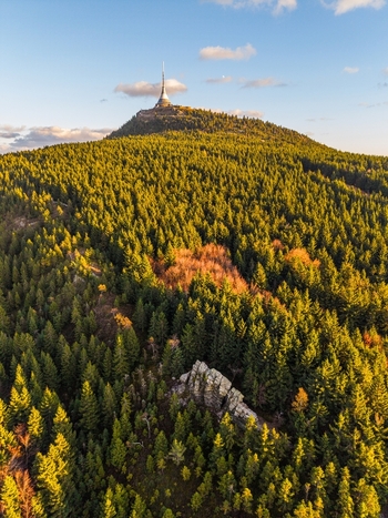 Aerial view of Jested Mountain and its tower above dense coniferous forest with a rock formation in the foreground during golden hour in Svetla pod Jestedem Liberec Region Czechia. Aerial view of Jested Mountain and its tower above dense coniferous forest with a rock formation in the foreground during golden hour in Svetla pod Jestedem Liberec Region Czechia.