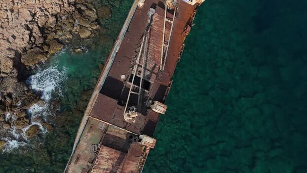 Aerial view of a rusted shipwreck off the rocky coast of Cyprus.