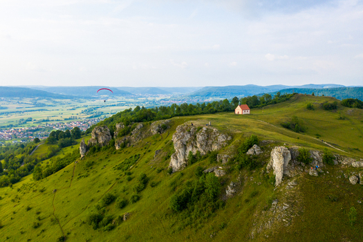Aerial view of Walberla mountain featuring the St. Walpurgis Chapel limestone rock formations and a paraglider soaring over the valley in Kirchehrenbach Bavaria Germany. Aerial view of Walberla mountain featuring the St. Walpurgis Chapel limestone rock formations and a paraglider soaring over the valley in Kirchehrenbach Bavaria Germany.