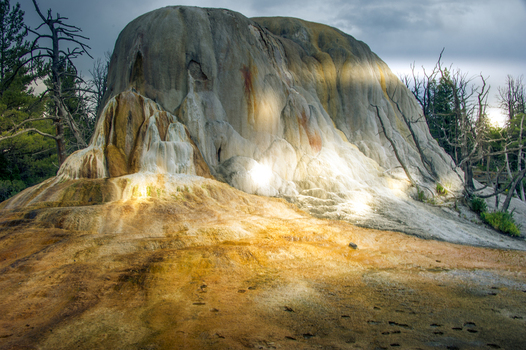 View of the travertine terraces at Mammoth Hot Springs with mineral deposits vibrant orange and white colors and surrounding dead trees in Yellowstone National Park United States.