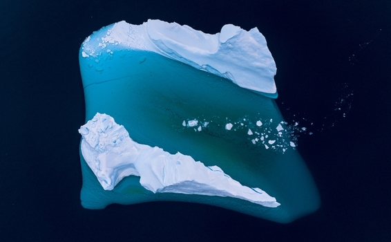 Aerial view of a massive iceberg with a vibrant turquoise submerged base floating in the dark blue Arctic waters in Tasiilaq Sermersooq Municipality Greenland. Aerial view of a massive iceberg with a vibrant turquoise submerged base floating in the dark blue Arctic waters in Tasiilaq Sermersooq Municipality Greenland.