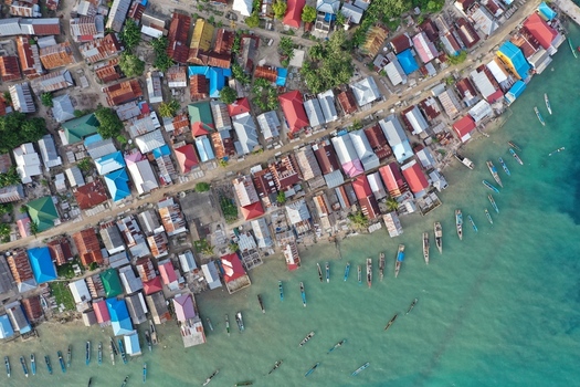 Aerial view of Pulau Maginti a dense coastal village with colorful rooftops and wooden fishing boats moored in the turquoise waters of Maginti South East Sulawesi Indonesia.