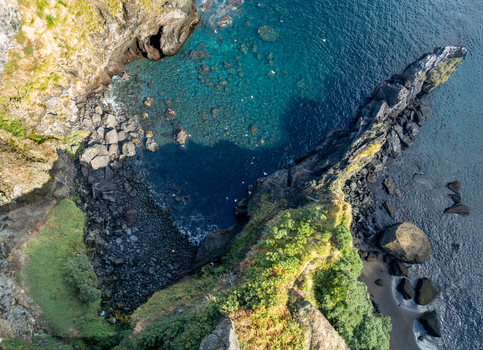 Aerial view of rugged cliffs and a sharp rock formation jutting into turquoise ocean waters Ribeira Grande Azores Portugal.