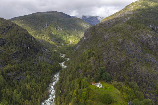 Aerial view of a winding river flowing through a lush valley surrounded by steep rocky mountains and dense forests Fjaera Vestland Norway. Aerial view of a winding river flowing through a lush valley surrounded by steep rocky mountains and dense forests Fjaera Vestland Norway.