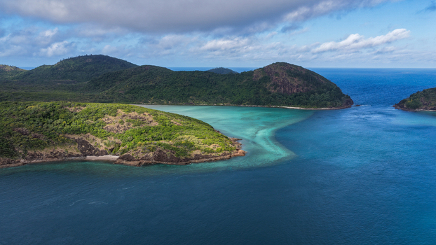Aerial view of Haslewood Island surrounded by turquoise waters coral reefs and lush green hills under a blue sky with scattered clouds in Whitsundays Queensland Australia. Aerial view of Haslewood Island surrounded by turquoise waters coral reefs and lush green hills under a blue sky with scattered clouds in Whitsundays Queensland Australia.