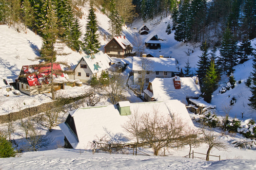 View of snow laden cabins nestling in a valley with evergreens and a landscape blanketed in white under a crisp winter sky Moce Banska Bystrica Region Slovakia.