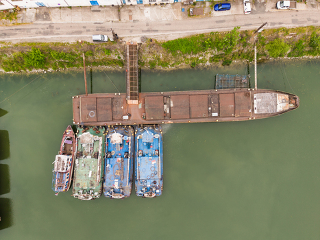 Aerial view of industrial barges and boats moored at a riverbank with a gangway and green water in Bratislava Bratislava Region Slovakia. Aerial view of industrial barges and boats moored at a riverbank with a gangway and green water in Bratislava Bratislava Region Slovakia.