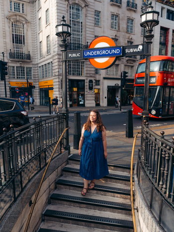 View of a woman in blue ascending from the iconic Underground past ornate railings and a red double decker bus London England United Kingdom. View of a woman in blue ascending from the iconic Underground past ornate railings and a red double decker bus London England United Kingdom.