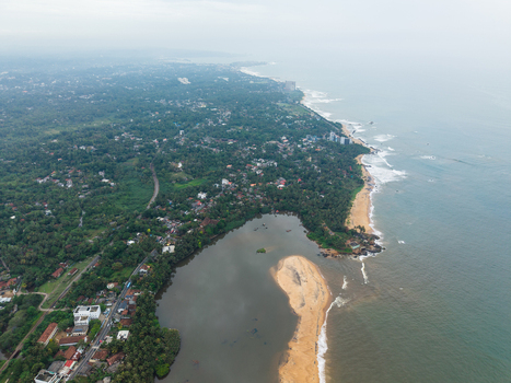Aerial view of the tropical coastline featuring a river mouth sandy beaches and lush green vegetation under an overcast sky in Galle Southern Province Sri Lanka. Aerial view of the tropical coastline featuring a river mouth sandy beaches and lush green vegetation under an overcast sky in Galle Southern Province Sri Lanka.