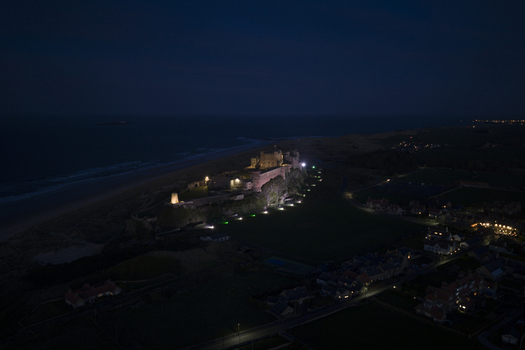 Aerial view of the illuminated Bamburgh Castle on the coast at night with village lights and the dark North Sea in Bamburgh England United Kingdom. Aerial view of the illuminated Bamburgh Castle on the coast at night with village lights and the dark North Sea in Bamburgh England United Kingdom.