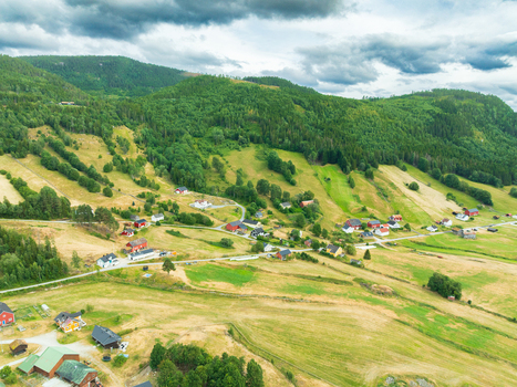 Aerial view of traditional wooden houses nestled among rolling green hills agricultural fields and dense forests in the rural village of Araksbo Agder Norway.