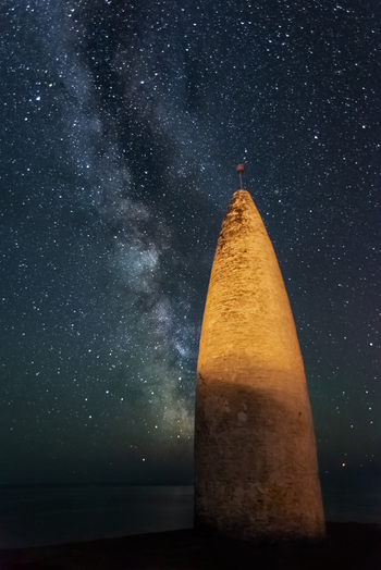 View of the Baltimore Beacon stone tower under the Milky Way and a starry night sky in County Cork Ireland.