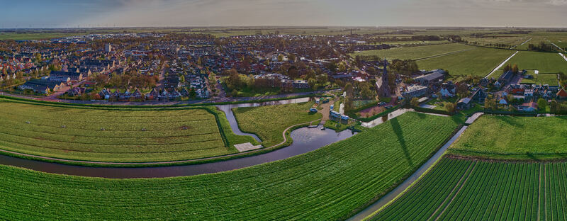Aerial view of the village center featuring a tall church spire surrounded by lush green fields and winding canals Spanbroek North Holland Netherlands.