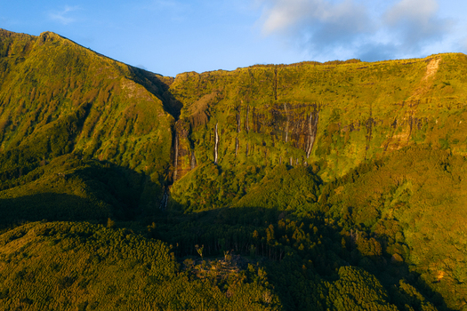 Aerial view of Poco da Ribeira do Ferreiro waterfalls cascading down lush green cliffs into a dense forest during golden hour Fajazinha Azores Portugal. Aerial view of Poco da Ribeira do Ferreiro waterfalls cascading down lush green cliffs into a dense forest during golden hour Fajazinha Azores Portugal.