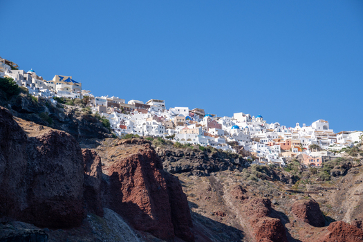 View of white houses and blue domed churches perched on the volcanic cliffs of Santorini under a clear blue sky in Fira Greece. View of white houses and blue domed churches perched on the volcanic cliffs of Santorini under a clear blue sky in Fira Greece.