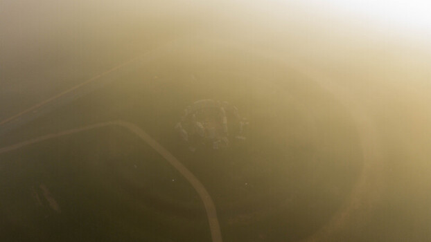 Aerial view of Stonehenge shrouded in thick morning fog with surrounding grassy landscape and ancient stone circles visible from above Salisbury England United Kingdom. Aerial view of Stonehenge shrouded in thick morning fog with surrounding grassy landscape and ancient stone circles visible from above Salisbury England United Kingdom.