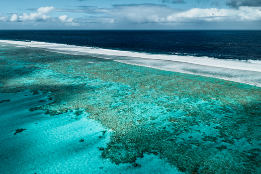 Aerial view of the Aitutaki coral reef with vibrant turquoise lagoon waters breaking waves along the barrier reef and the deep blue Pacific Ocean in the Cook Islands. Aerial view of the Aitutaki coral reef with vibrant turquoise lagoon waters breaking waves along the barrier reef and the deep blue Pacific Ocean in the Cook Islands.