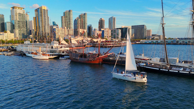 Aerial view of the San Diego skyline and harbor featuring the historic Star of India tall ship and a modern sailboat docked along the North Embarcadero in San Diego California United States.