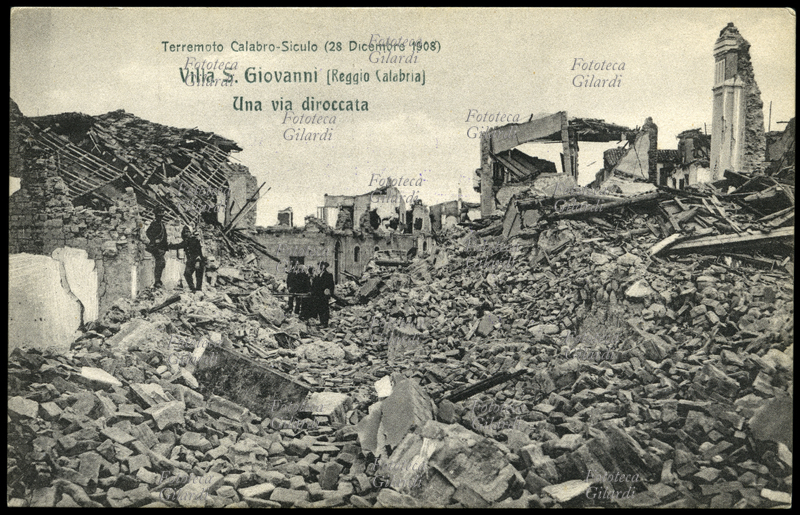 TERREMOTO Calabro-Siculo del 1908. Villa San Giovanni (Reggio Calabria) una via diroccata. Superstiti e soccorritori si aggirano fra le macerie, che potrebbero serbare ancora i corpi dei dispersi, oltre che qualche oggetto di uso quotidiano ancora recuperabile. Il terribile sisma di magnitudo 7,2 ha contato fra le 90.000 e le 120.000 vittime in tutta la zona colpita. Cartolina postale da una serie edita dalla Croce Rossa a sottoscrizione per i terremotati, sistema mediatico pionieristico per la raccolta dei fondi a favore delle vittime di catastrofe naturale, che nell\
