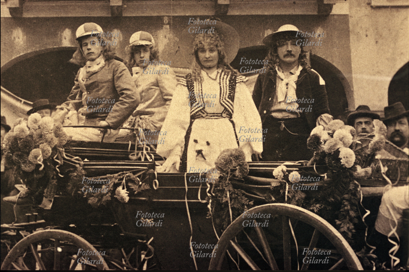CARNEVALE carro tradizionale decorato con fiori e stelle filanti. A bordo quattro personaggi con le maschere tradizionali in posa a beneficio del fotografo [dettaglio; intero al Web ID 30692]. Fotografia virata seppia, Italia 1910 circa.