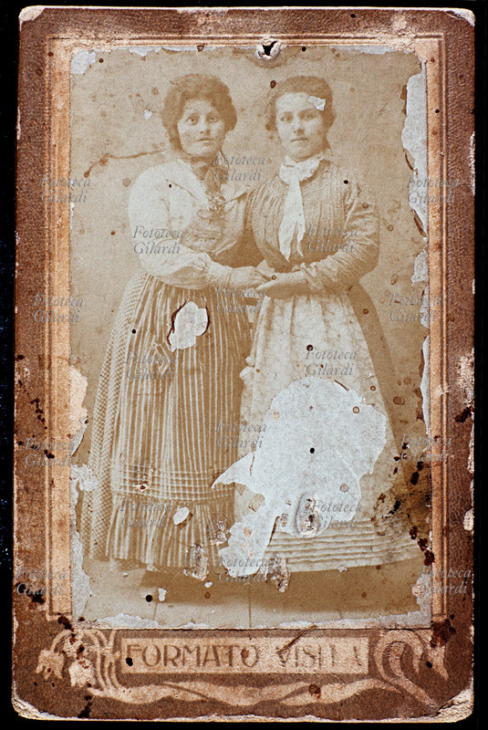 FAMIGLIA due donne posano in atelier, probabilmente sorelle o cugine, si tengono per mano e sorridono. Fotografia di anonimo eseguita in studio, formato Visita, Italia 1880 circa.