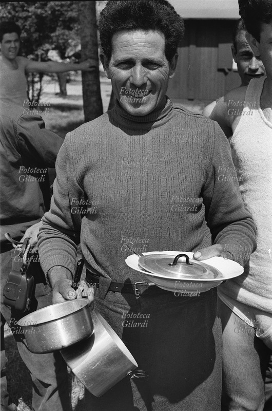 EMIGRAZIONE Italia Germania. Lavoratore italiano davanti al locale mensa con in mano piatto e pentola per cucinare gli spaghetti, alimento tipicamente italiano. Fotografia Ando Gilardi, 1960