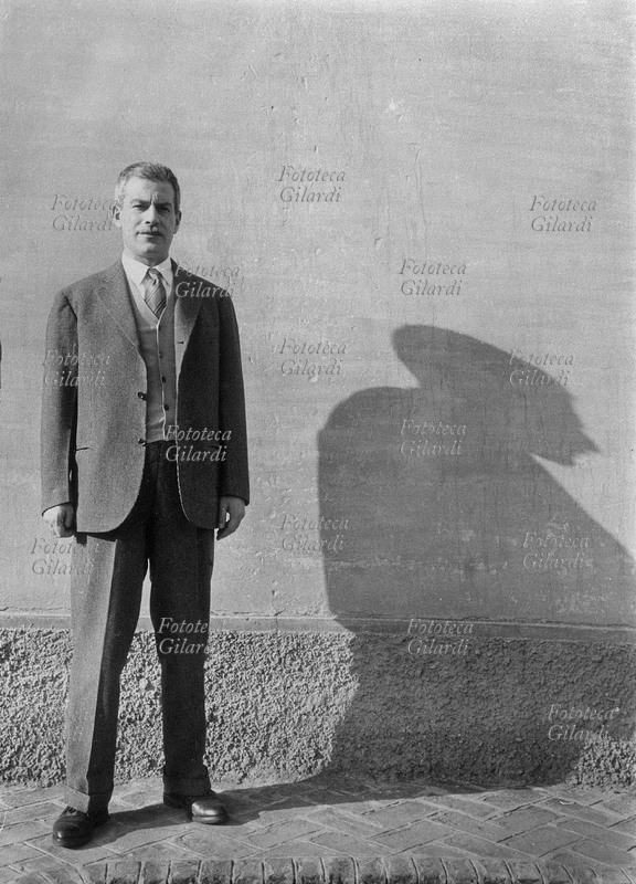 Elio VITTORINI (1908-1966) scrittore, ritratto a figura intera dinnanzi ad un muro che proietta la sua ombra, 1960 circa.