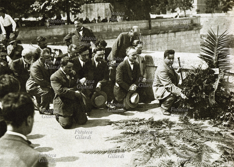 Giacomo MATTEOTTI (1885-1924) Un gruppo di aventiniani: gli onorevoli Gino Baldesi (1879 – 1934), Alessandro Bocconi (1873 – 1960), Antonio Priolo (1891 – 1978), Arturo Labriola (1873 – 1959), Emilio Caldara (1868 – 1942), Camillo Prampolini (1859 – 1930), Cassinelli e Enrico Gonzales (1882 – 1965) depongono una corona sul luogo dove Matteotti è stato rapito, che la gente ha già omaggiato di foglie di palma, simbolo del martirio qui parafrasato in ambito politico. Italia, 1924.