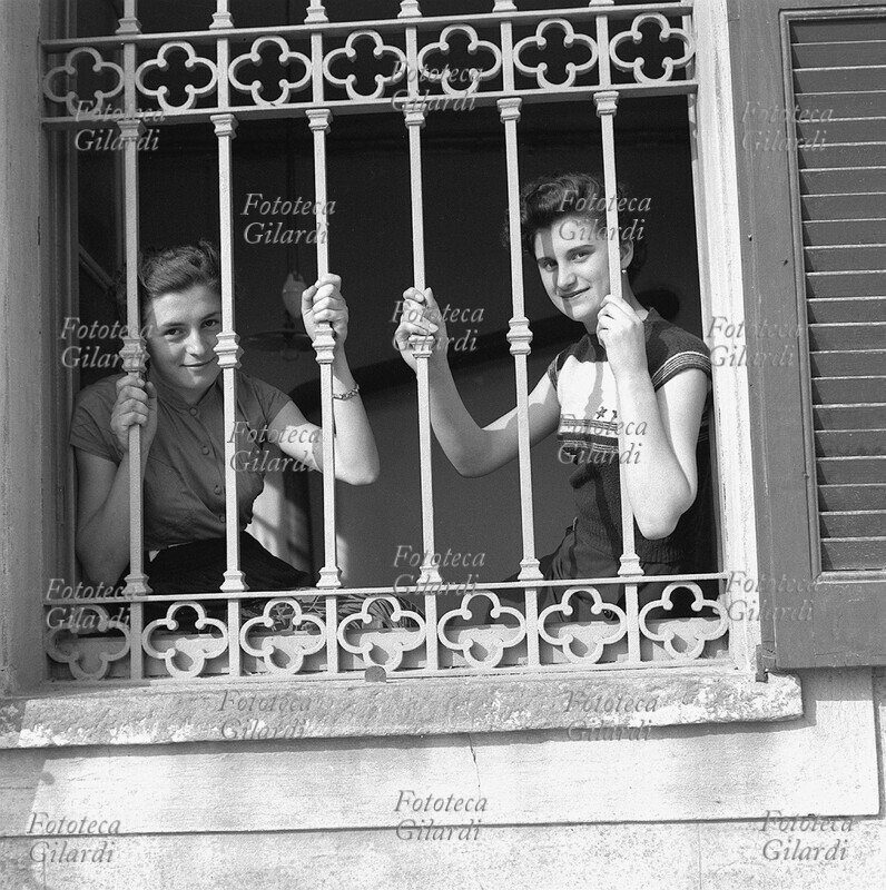 STORIA DEL MOVIMENTO OPERAIO giovani lavoratrici del Cotonificio Valle Ticino, ritratte attraverso una finestra inferriata dello stabilimento, nel corso delle lotte contro la smobilitazione ed i licenziamenti. Fotografia di Ando Gilardi (1921 - 2012) #andogilardi, Italia, Turbigo (Milano) 1953.