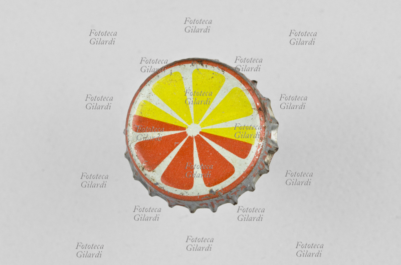 TAPPO A CORONA, capsula metallica di chiusura per bottiglia o bottiglietta di vetro per limonata o aranciata, decorata con la stilizzazione su fondo bianco di una sezione di agrume colorato metà in giallo e metà in arancio come il cerchio che chiude la circonferenza; sulla gonna argentata si intravede la scritta arancio \
