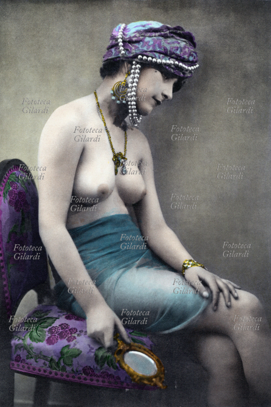 EROTISMO giovane donna in costume da odalisca, a seno nudo con turbante adornato di perle, in mano regge uno specchio. Il fascino dell\
