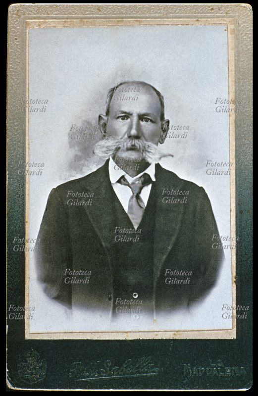 MODA maschile. Uomo anziano in giacca e cravatta, accessori, capigliatura scarsa ma lunghi e folti baffi bianchi. Fotografia R.A. Sabella, La Maddalena (Sassari) 1920 circa.