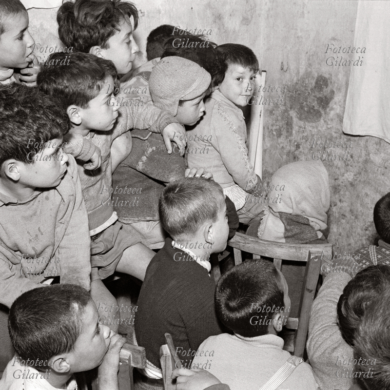 DOPOSCUOLA a cortile Scalilla, scolari attenti alla lezione, tenuta in questo caso sottoforma di piccolo spettacolo di pupazzi, dai coniugi Michela e Goffredo Fofi. Fotografia di Ando Gilardi (1921 - 2012) #andogilardi da ampio servizio; Palermo, 1957.Questa immagine è inclusa nel nostro fotolibro in vendita qui.