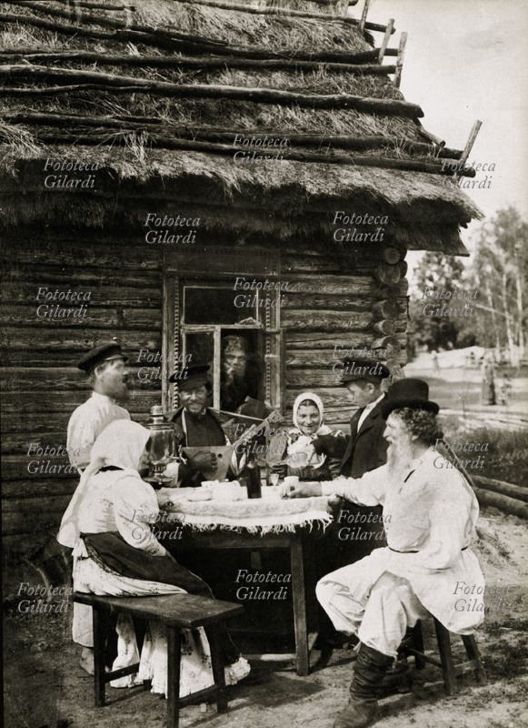 RUSSIA paesani bevono tè, vodka e cantano accompagnati da un suonatore di balalaika, seduti attorno ad un tavolo davanti ad una \