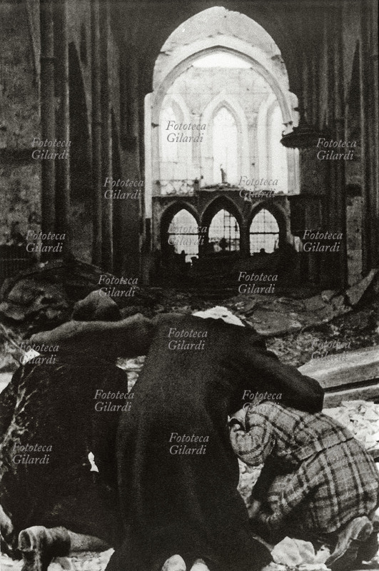 II GUERRA MONDIALE Bombardamento di Berlino: una famiglia tedesca inginocchiata di fronte ad una cattedrale sventrata dalle bombe. Germania 1945.